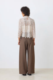Back view of a woman wearing a lines long sleeve beige lace blouse paired with brown trousers