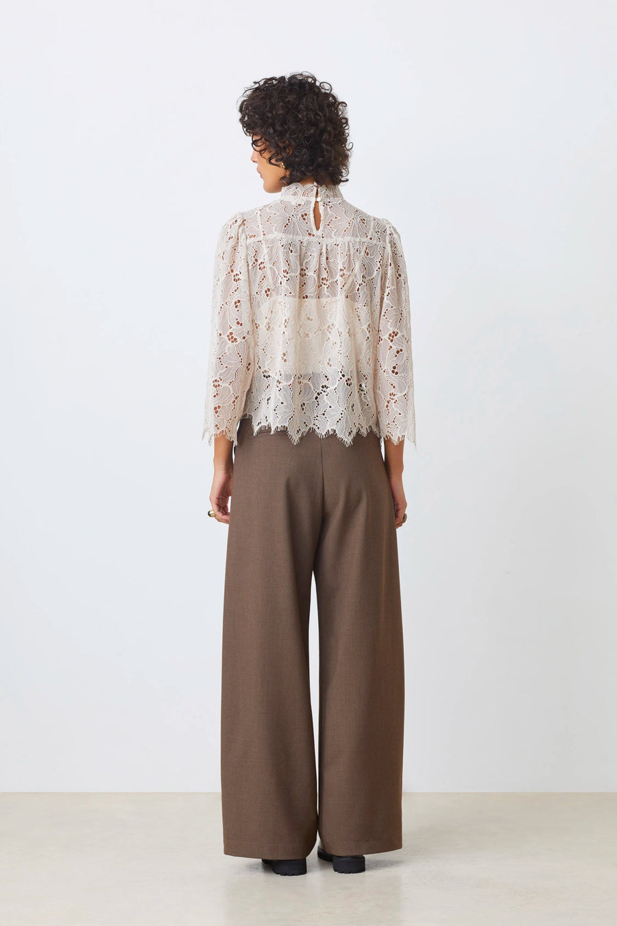 Back view of a woman wearing a lines long sleeve beige lace blouse paired with brown trousers