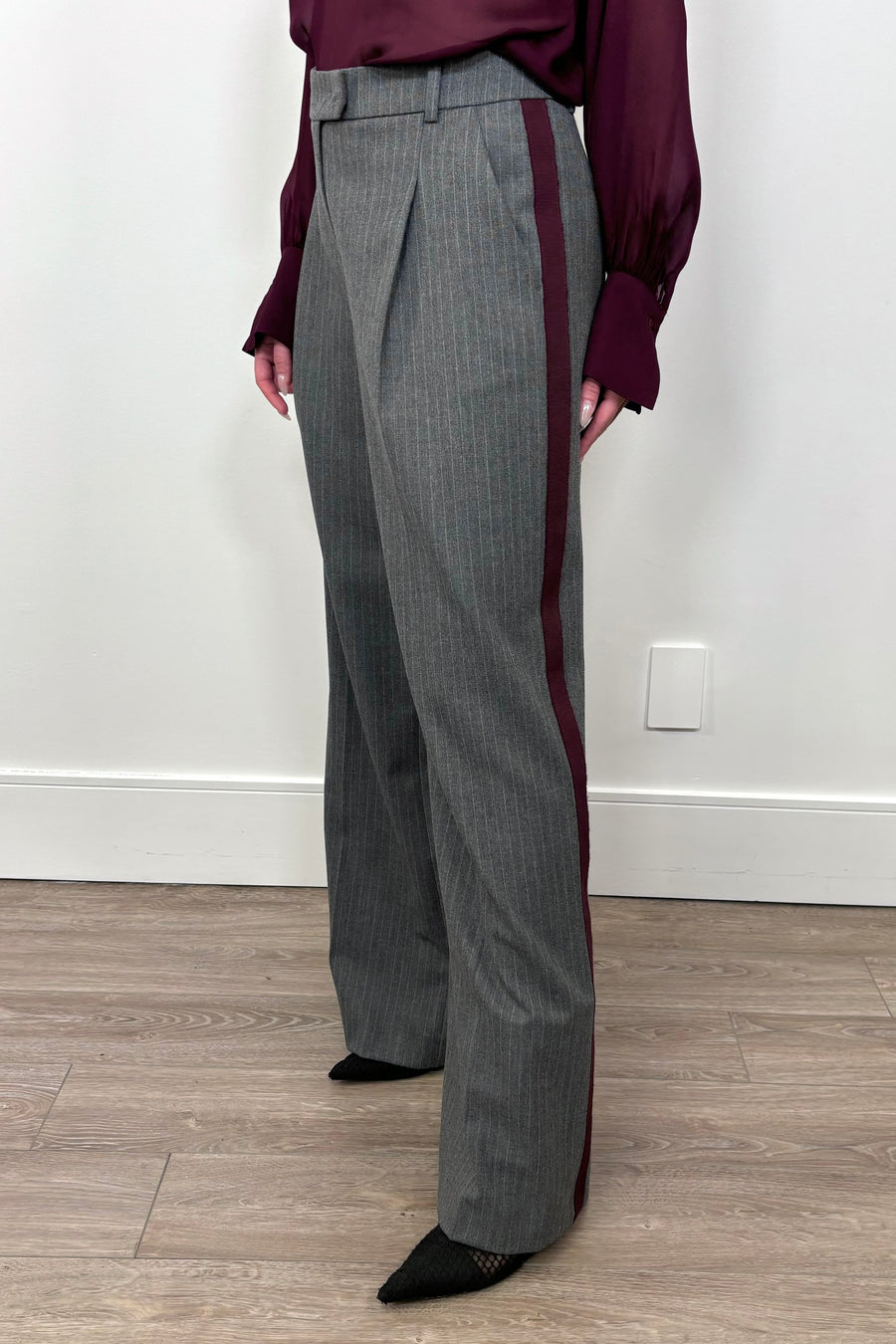 3/4 view of woman wearing a gray pinstripe wide leg pant with a burgundy line down the leg