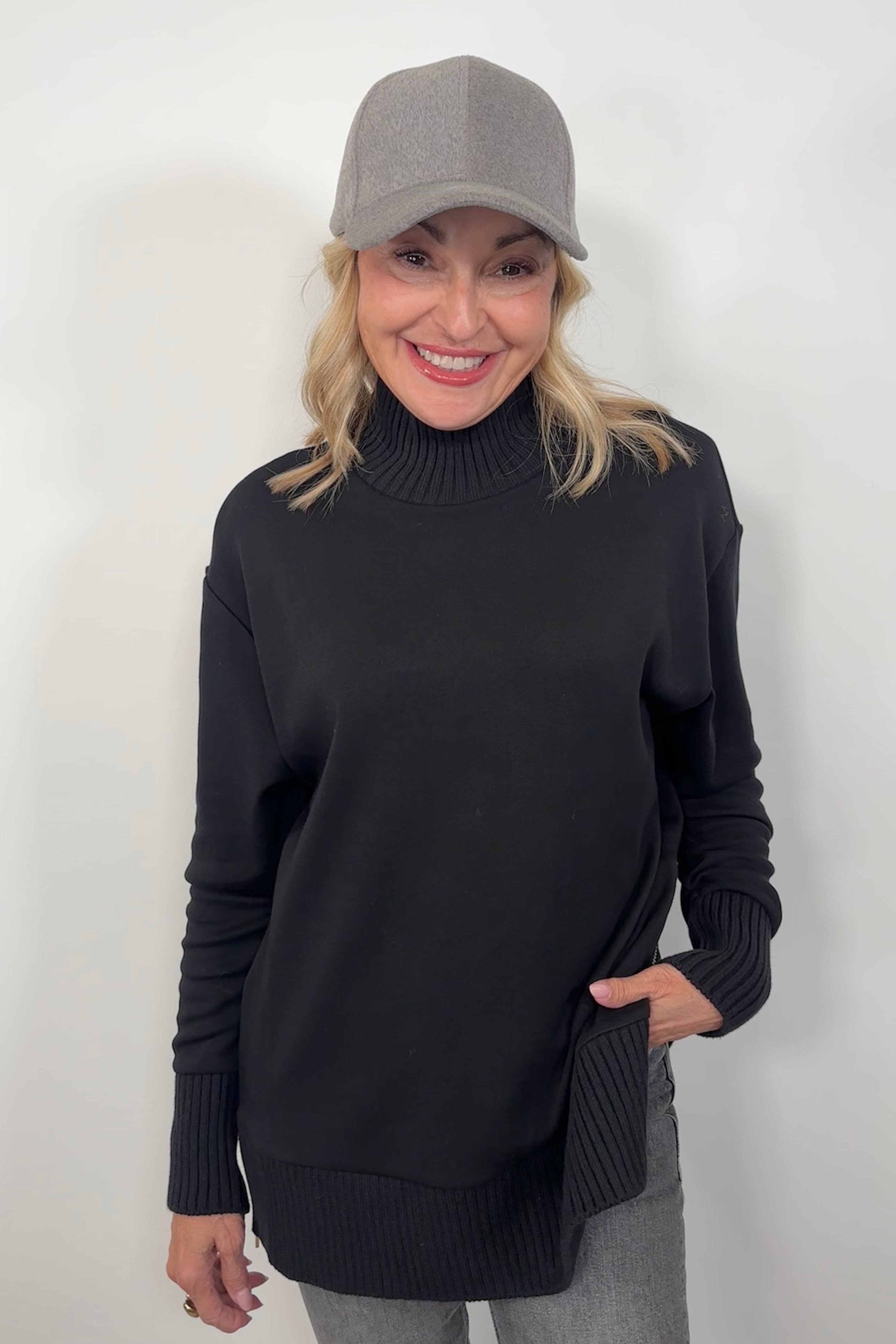 Woman wearing a black mock neck sweater and gray cap against a white background