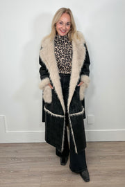 Front view of a woman wearing an open long black coat with fur detailing and hem on the collar, pockets and belt.