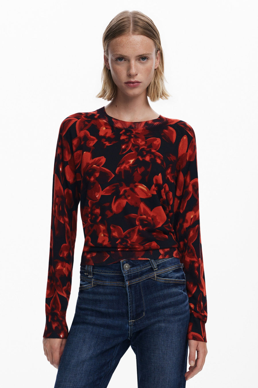 Woman wearing a red and black floral long-sleeve top and blue jeans on a white background