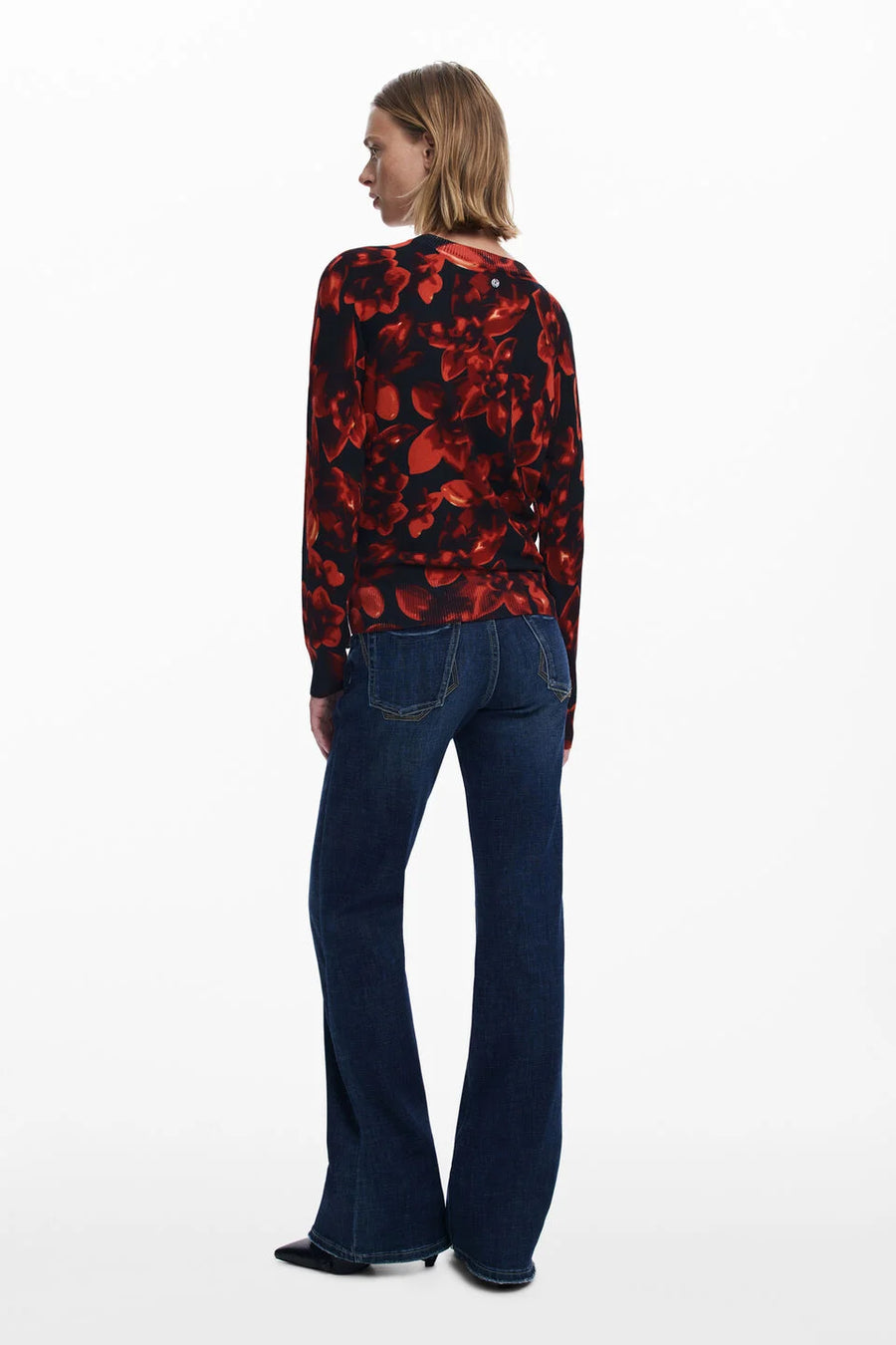 Person wearing a red and black floral sweater with blue jeans on a white background