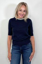 Front view of woman wearing a navy knitted top with pearl detailing in the neck