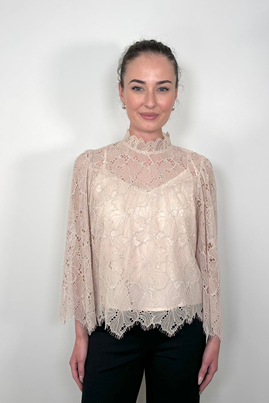 Front view of a woman wearing a lined long sleeve beige lace blouse