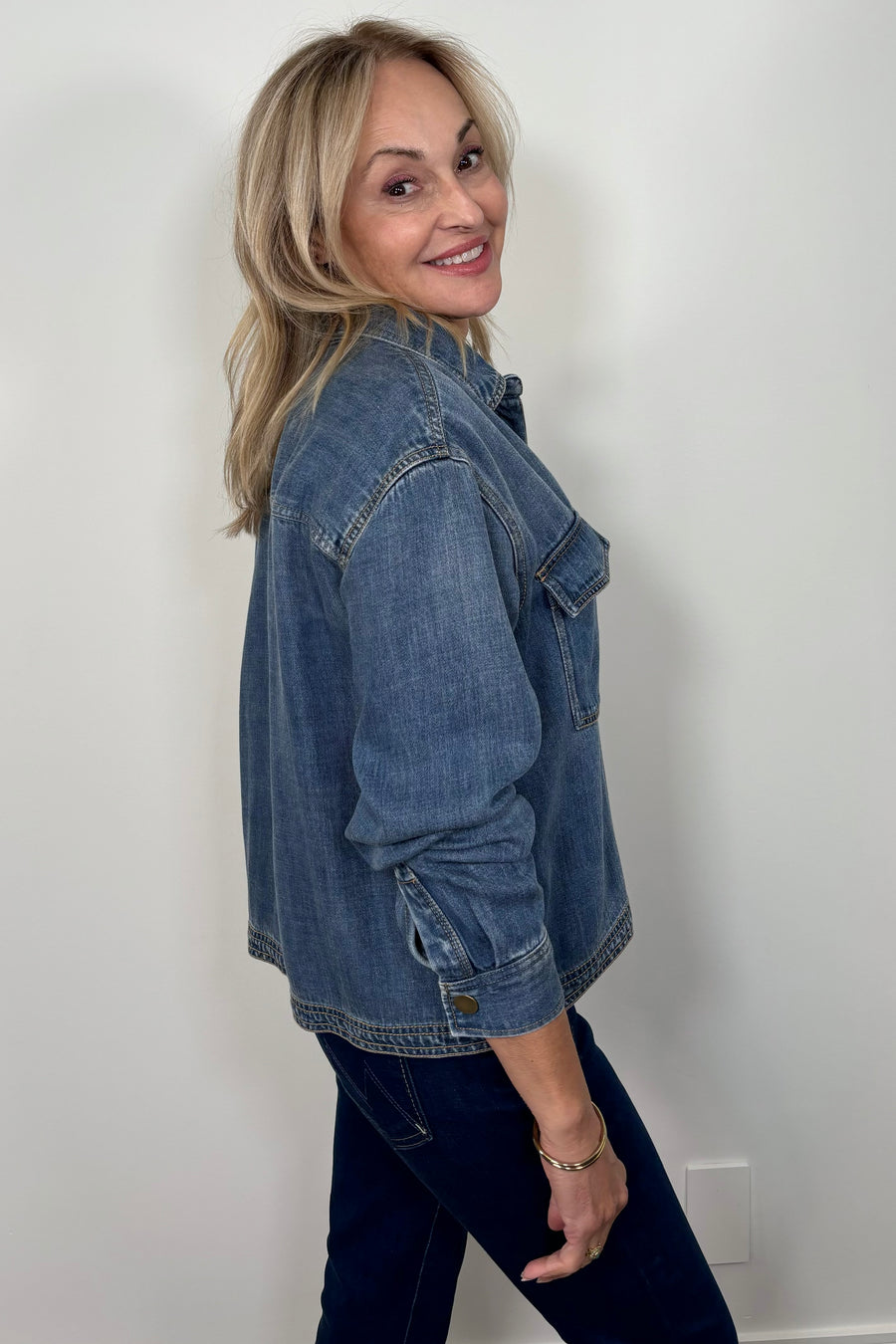 Side view of a woman wearing a relaxed blue denim long sleeve shirt