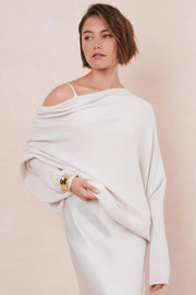 Woman wearing a white off-shoulder sweater against a beige background
