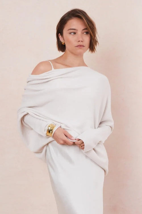 Woman wearing a white off-shoulder sweater with a plain background