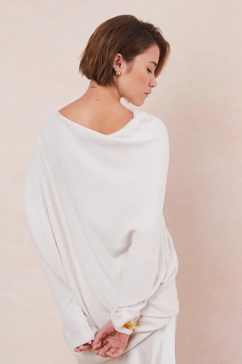 Woman wearing a white off the shoulder sweater and pants against a beige background