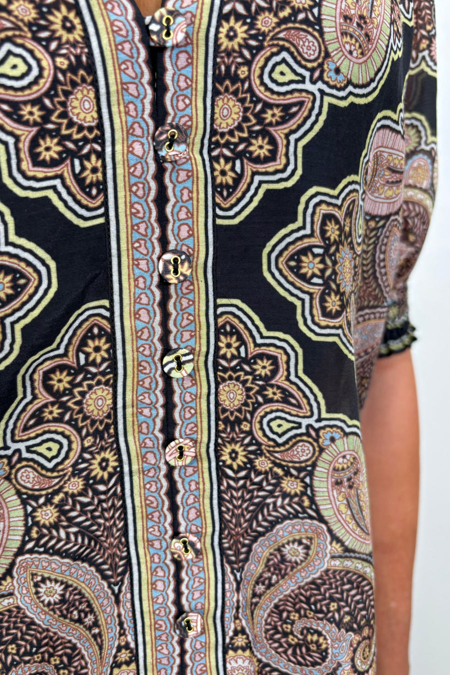 Zoom in of a woman’s torso wearing a cotton and silk blend black half sleeve top with a light brown pattern