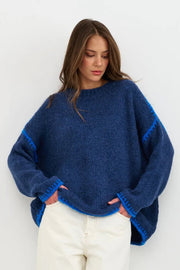 Woman wearing a blue sweater with white pants against a white background
