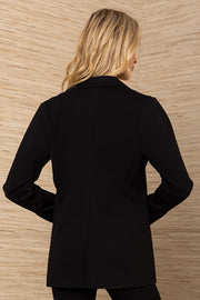 Woman wearing a black blazer standing against a wooden paneled wall.