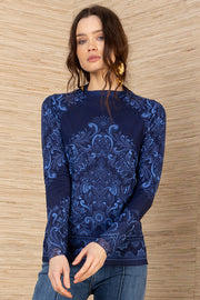 Woman wearing a blue patterned mesh turtleneck and blue jeans against a wooden wall.