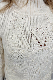 Close-up of a cream-colored knitted sweater with intricate patterns.