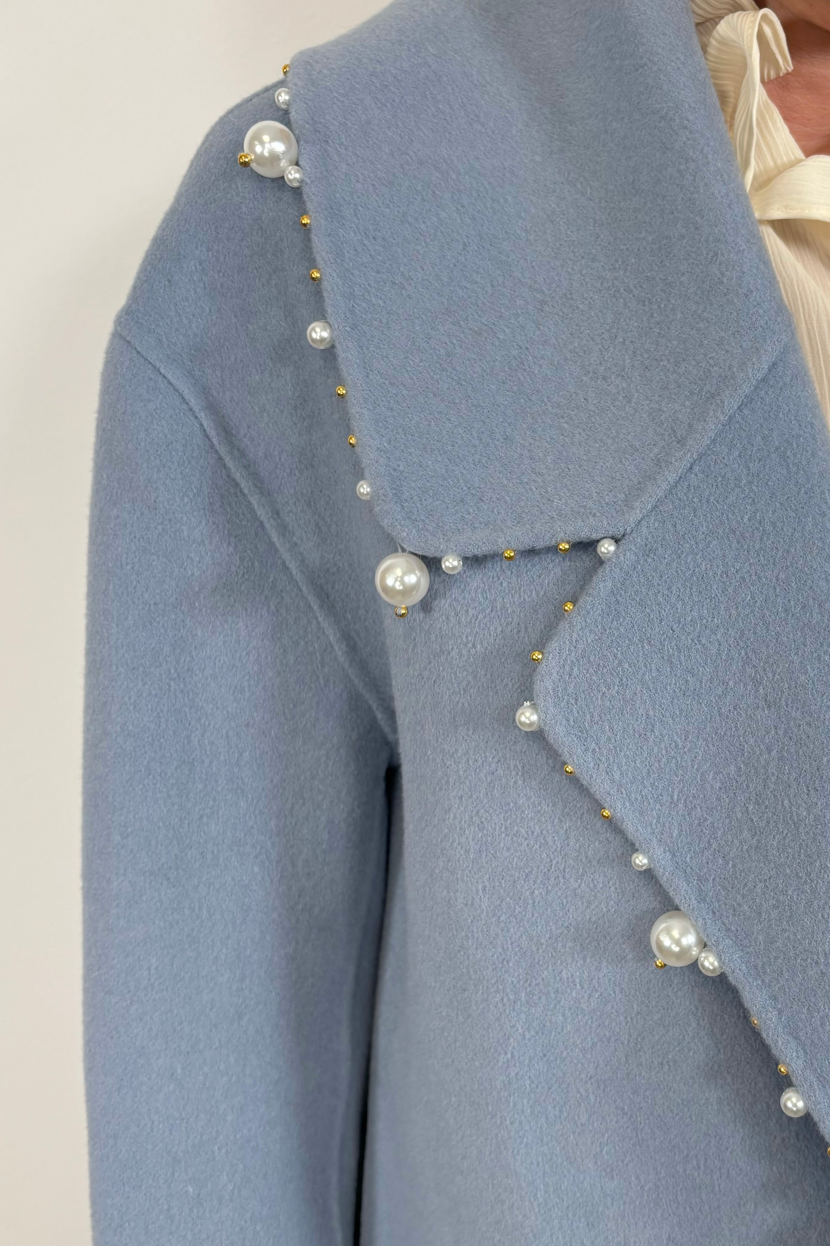 Close-up view an oversized blue blazer with pearl detailing on the trim paired