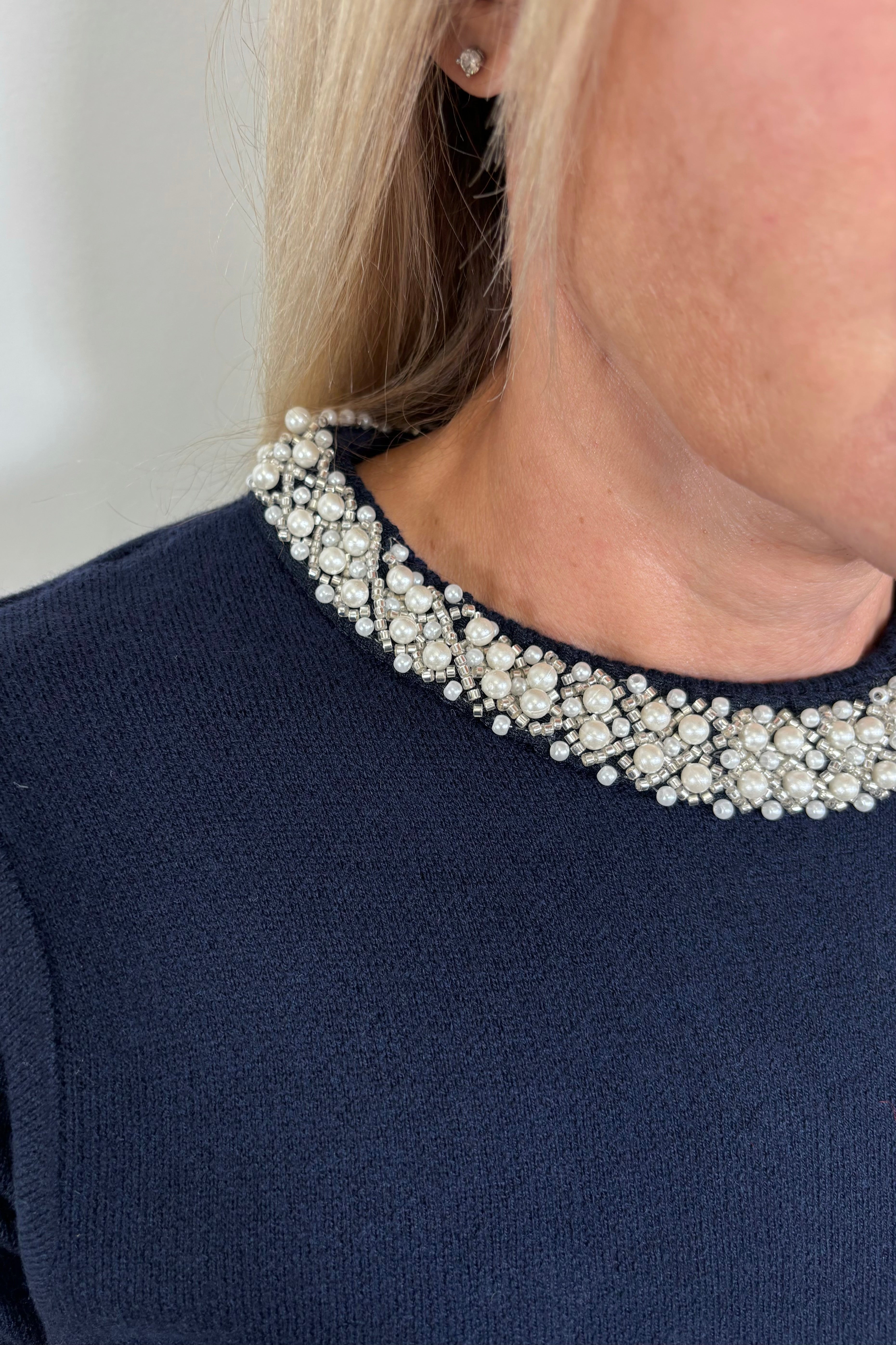 Zoom in of woman wearing a navy knitted top with pearl detailing in the neck