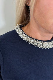 Zoom in of woman wearing a navy knitted top with pearl detailing in the neck