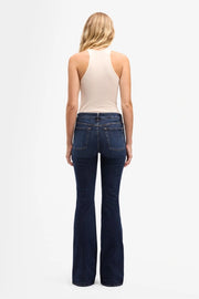 Person wearing blue flared jeans and a beige tank top on a white background