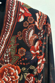 Close-up of a floral and paisley patterned fabric with red, green, and white colors on a black background.
