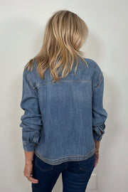 Back view of a woman wearing a relaxed blue denim long sleeve shirt