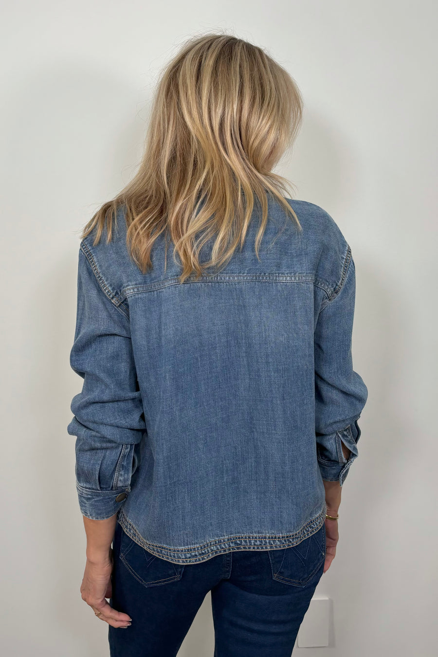 Back view of a woman wearing a relaxed blue denim long sleeve shirt