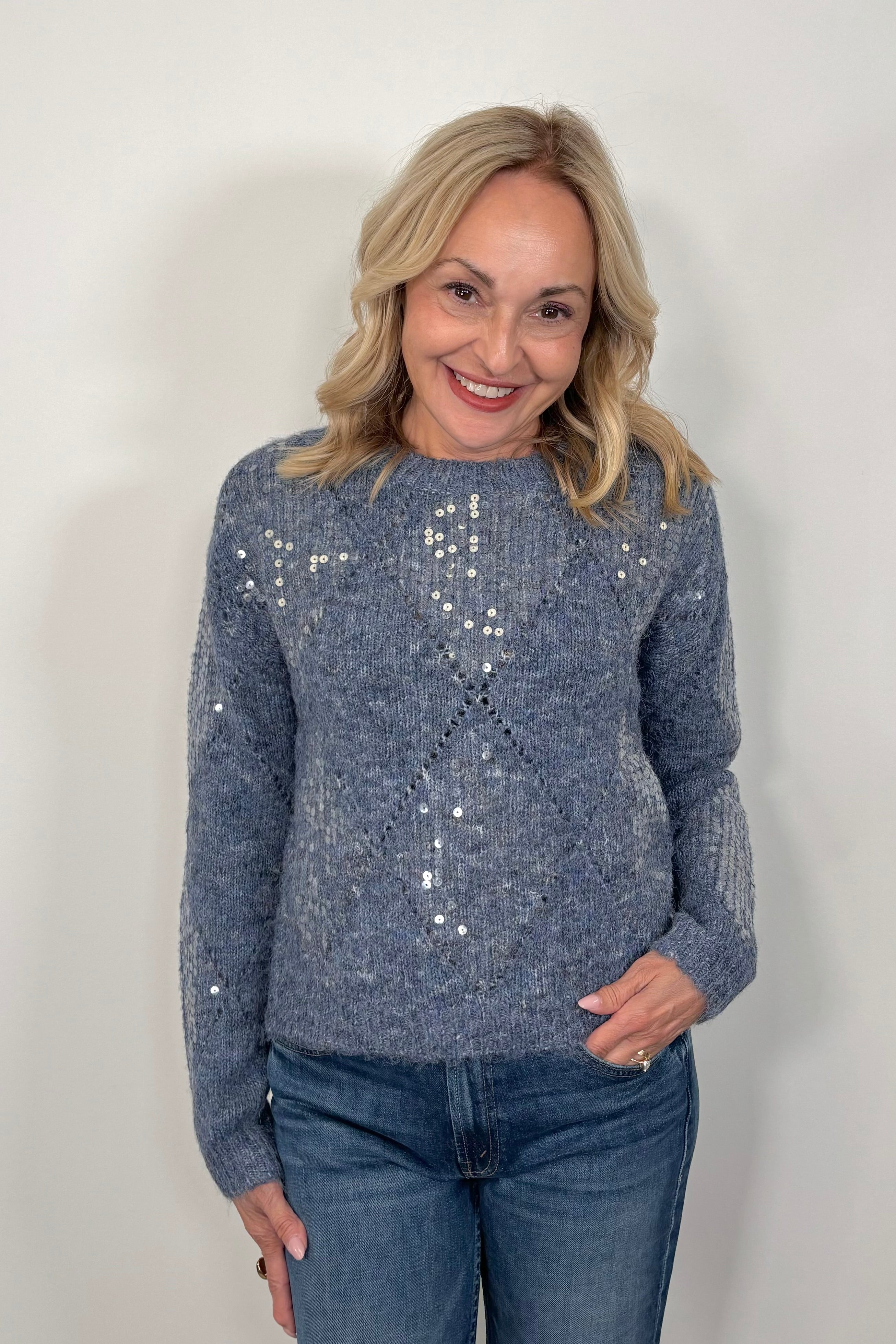 Woman wearing a blue diamond sequin pattern sweater against a white background