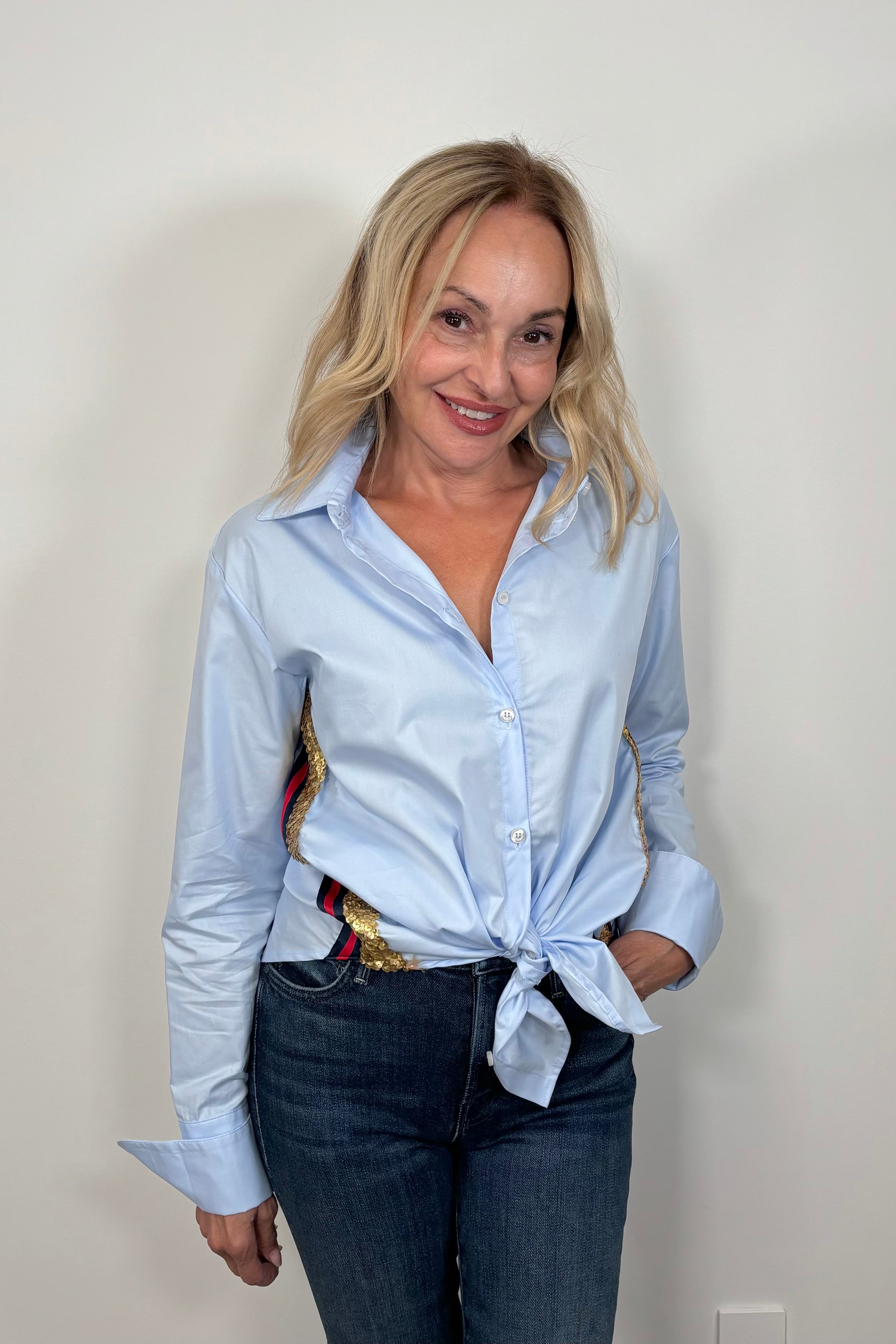 woman wearing a light blue shirt with red, navy and gold sequence stripes on the side