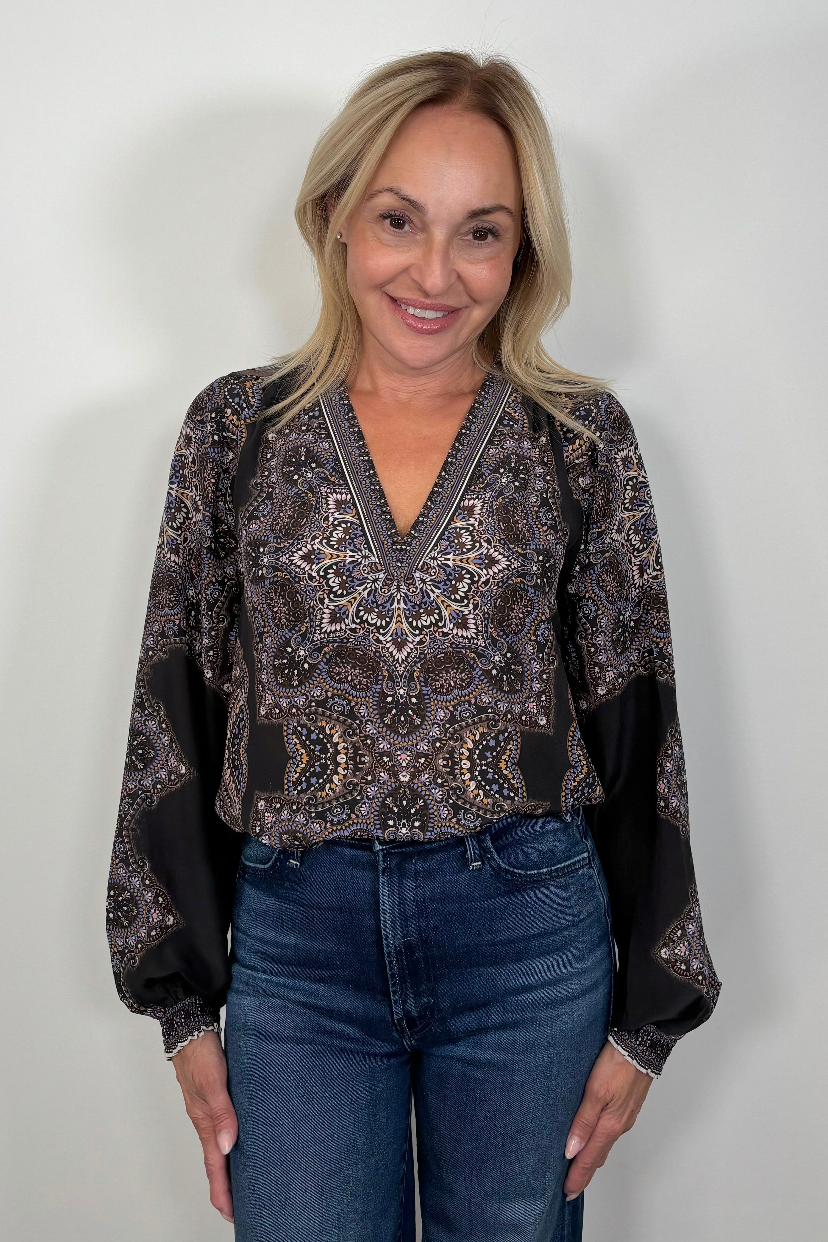 Front view of woman wearing a cuffed blouson sleeved patterned black blouse tucked in