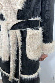 Close up view of the belt of an open long black coat with fur detailing and hem on the collar, pockets and belt.