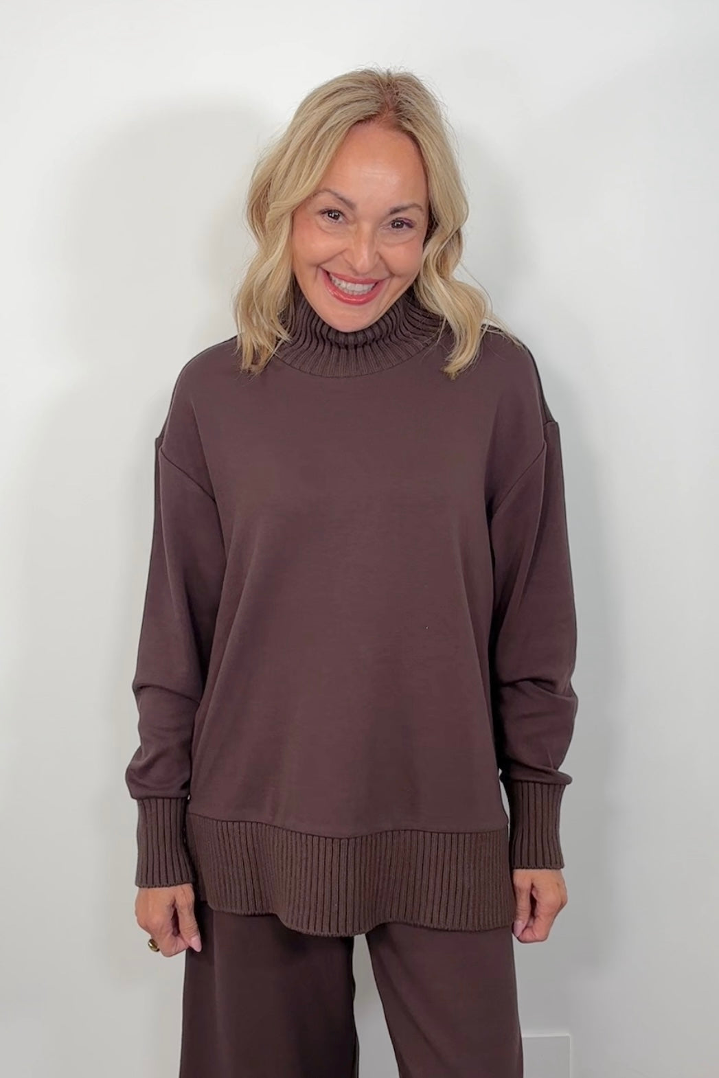 Woman wearing a brown sweater and pants against a white background