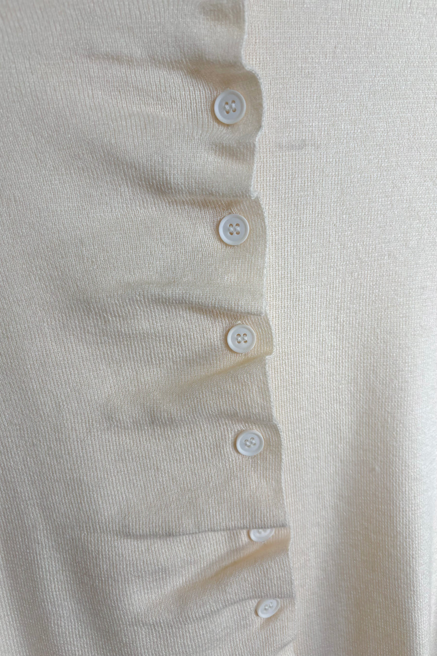 Front zoom in view of a rouched in the buttons cream long sleeve knitted top
