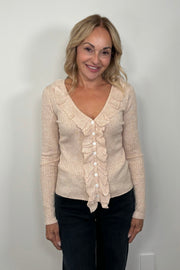 Front facing woman wearing an oat  coloured v-neck with ruffles long sleeve ribbed top.