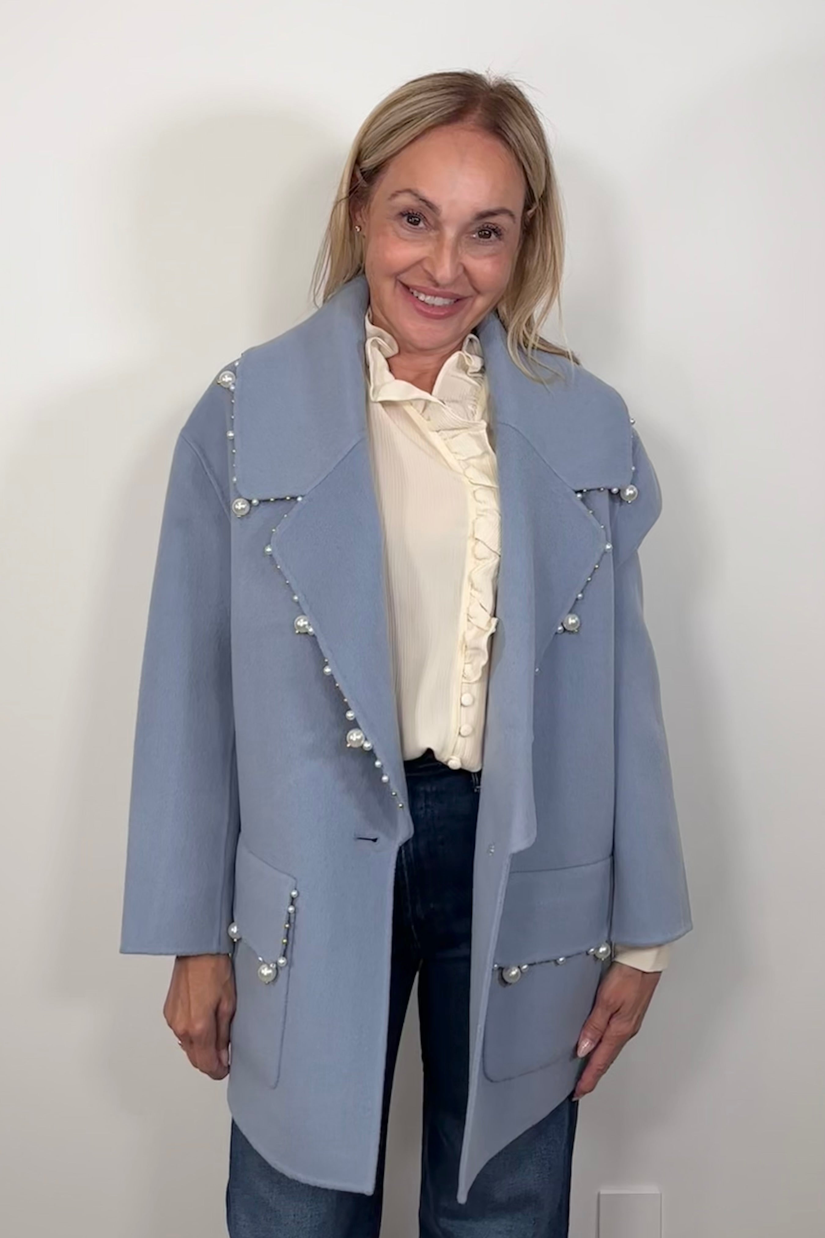 Front view of woman wearing an oversized blue blazer with pearl detailing on the trim paired with a off white blouse and jeans