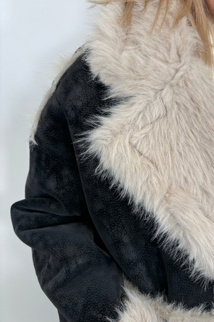 Close up view pf the collar of a long black coat with fur detailing and hem on the collar, pockets and belt.