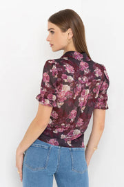 Back view of woman wearing a black and pink floral blouse and jeans on a white background