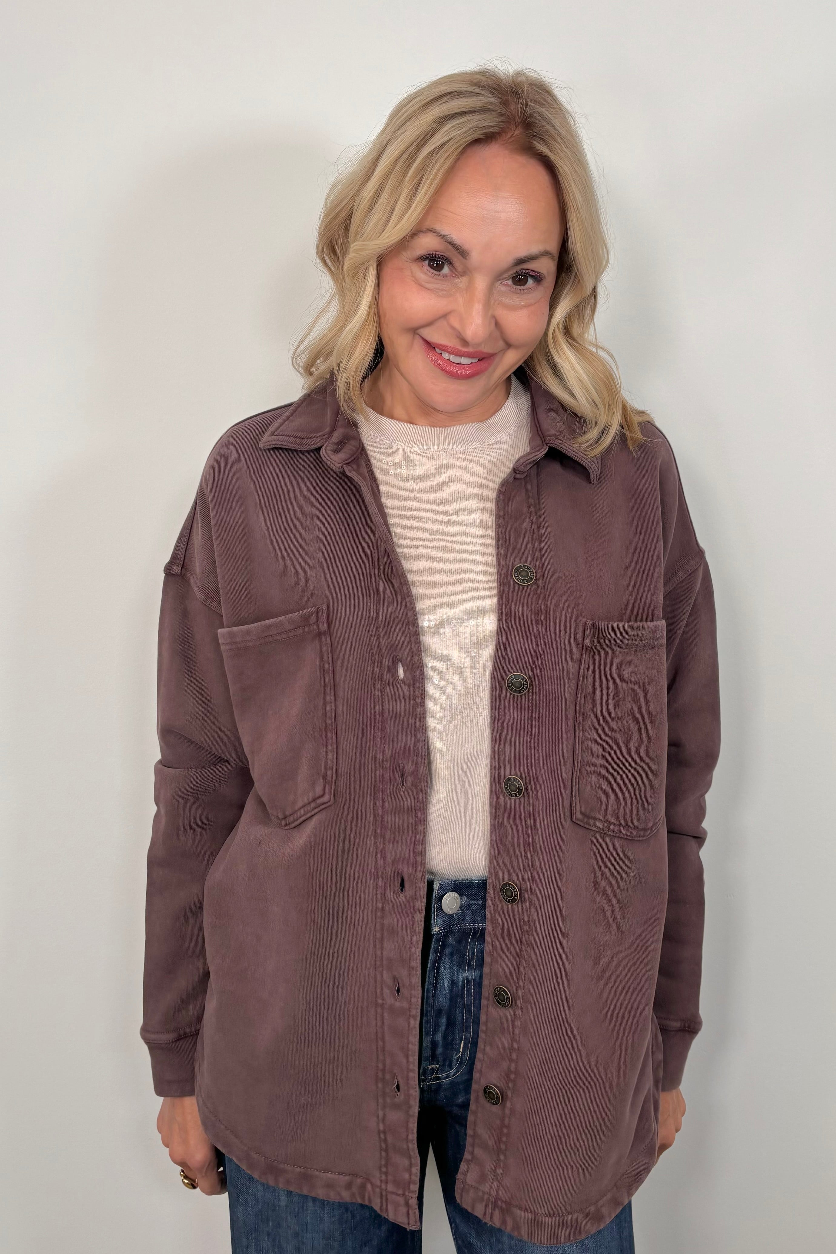 Woman wearing a brown jacket over a white sweater and blue jeans against a white background