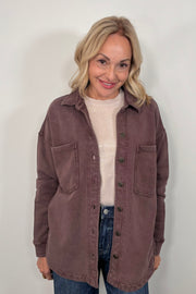Woman wearing a brown jacket over a white sweater and blue jeans against a white background