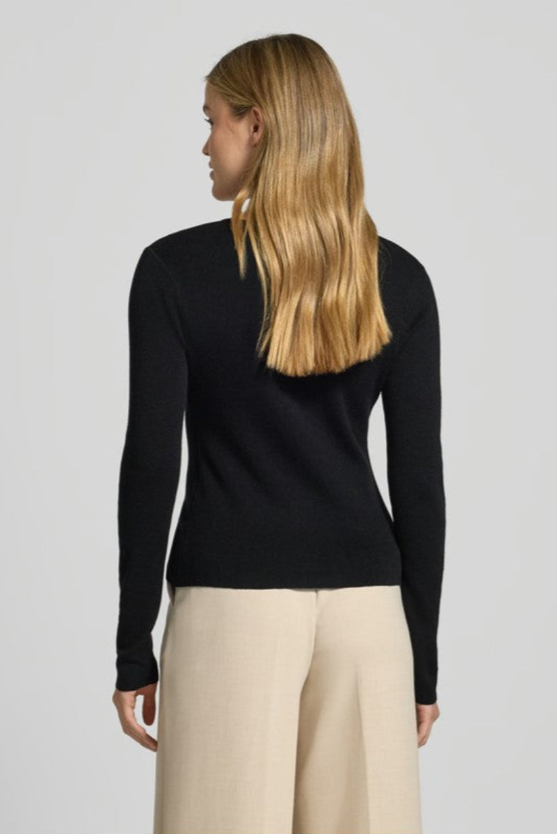 Person wearing a black long-sleeve top and beige pants on a light gray background