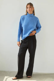 Person wearing a blue sweater and black pants against a plain background