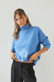 Woman wearing a blue sweater and black pants against a plain background