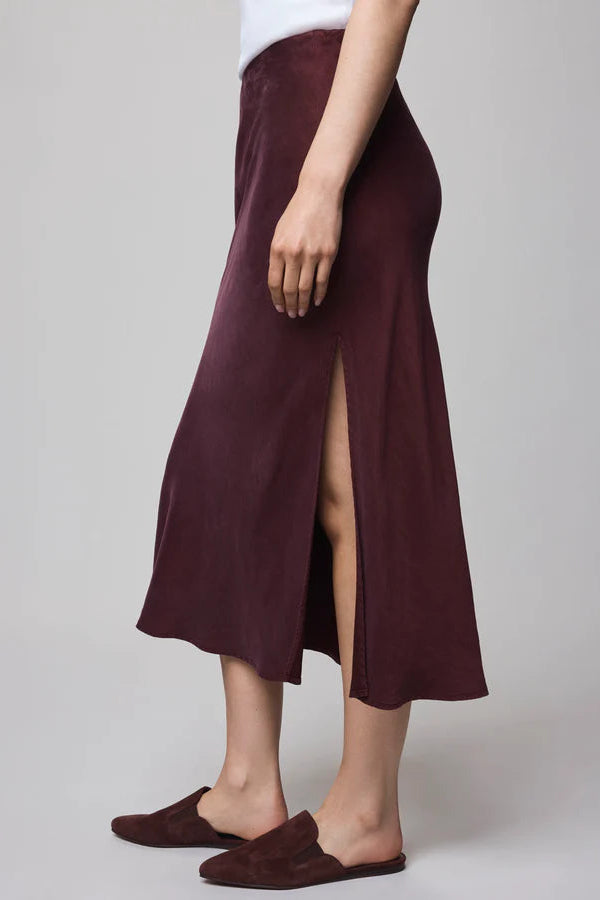 Person wearing a burgundy skirt with a high slit on a plain background