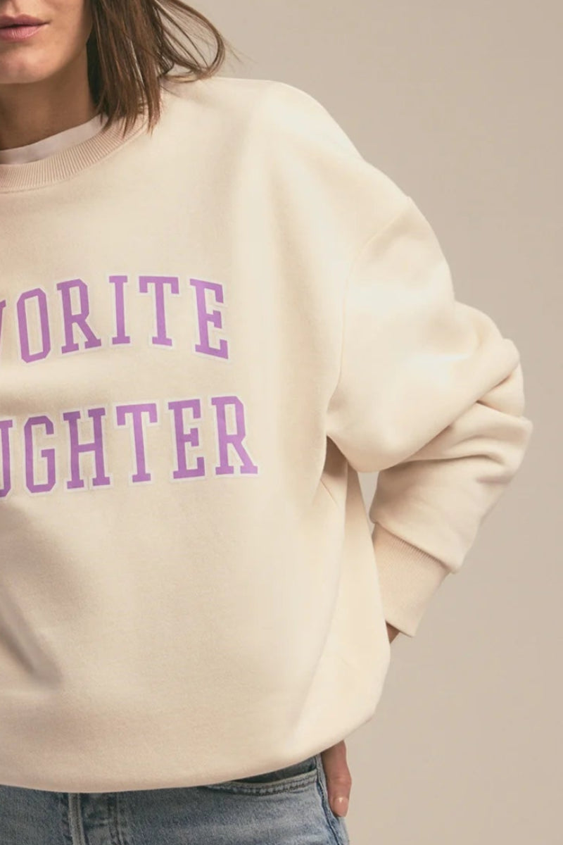 Woman wearing a beige sweatshirt with 'Favorite Daughter' text on a plain background
