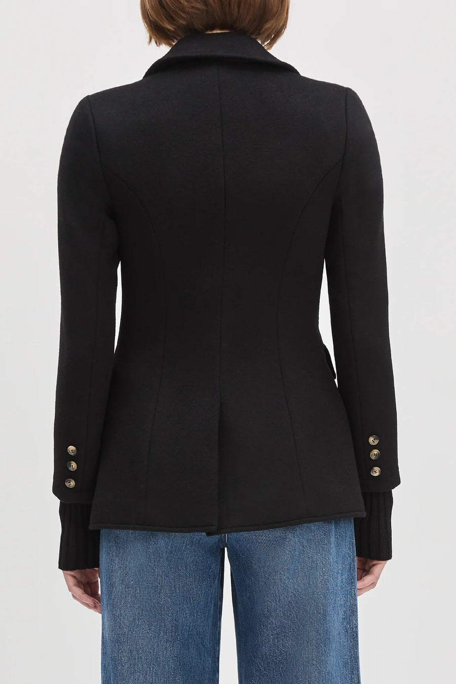 Back view of a woman wearing a black jacket with cuff sleeves, brown top and black jeans