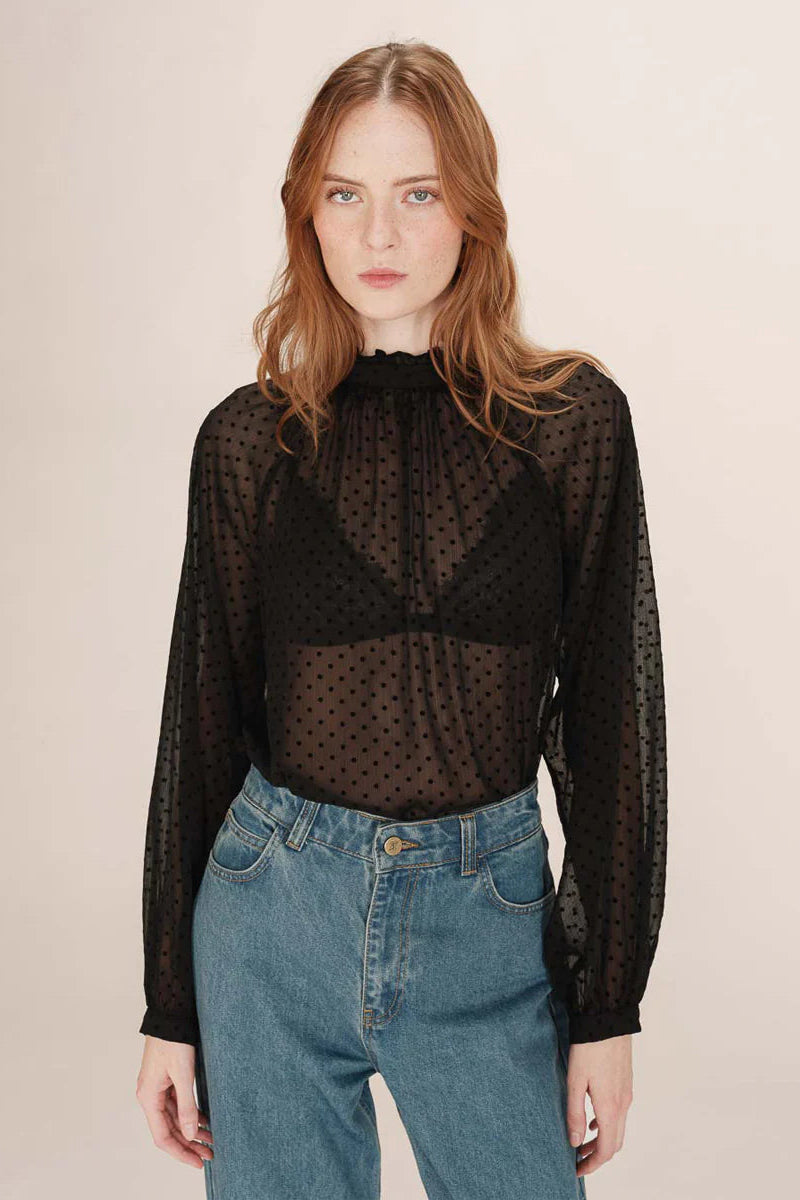 Woman wearing a sheer black polka dot blouse and blue jeans