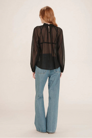 Woman wearing a sheer black polka dot blouse and blue jeans