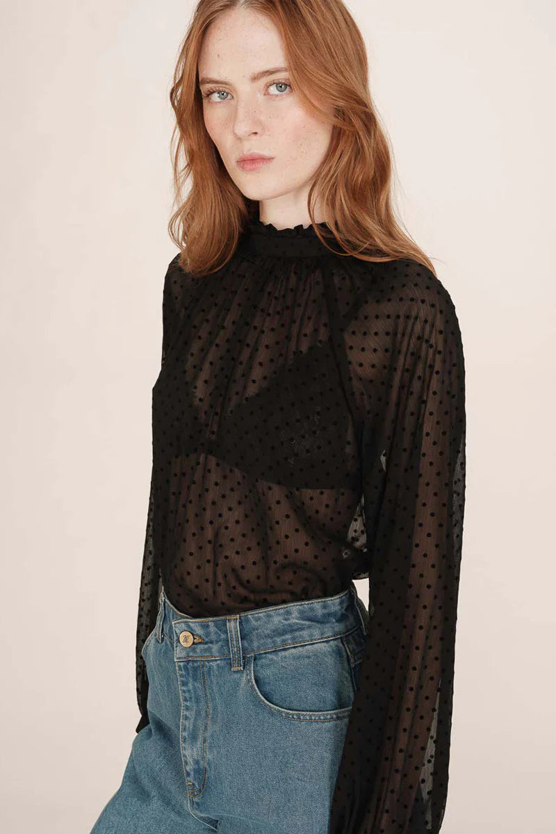 Woman wearing a sheer black polka dot blouse and blue jeans