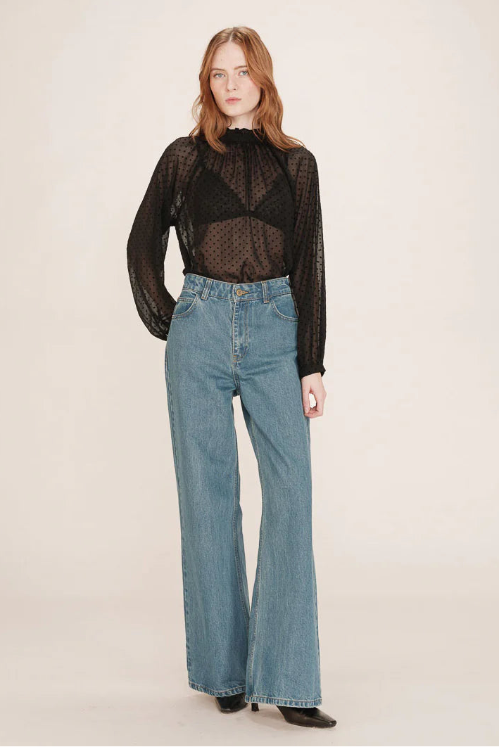 Woman wearing a black sheer top and blue jeans on a white background