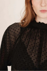Woman wearing a sheer black polka dot blouse and blue jeans