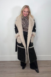 Video of a woman wearing an open long black coat with fur detailing and hem on the collar, pockets and belt.