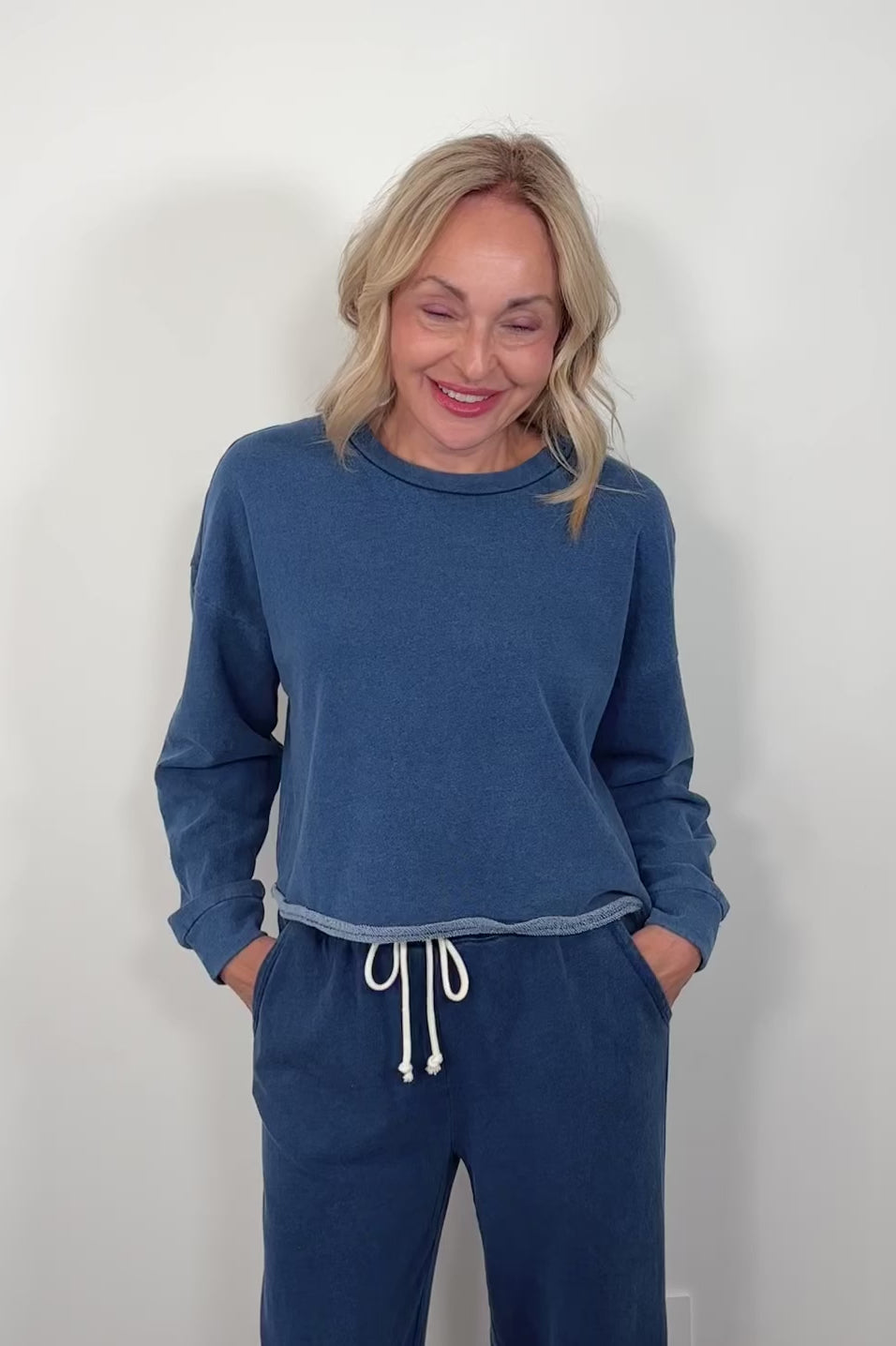 video of a woman wearing a blue sweatshirt and matching pants with a white background